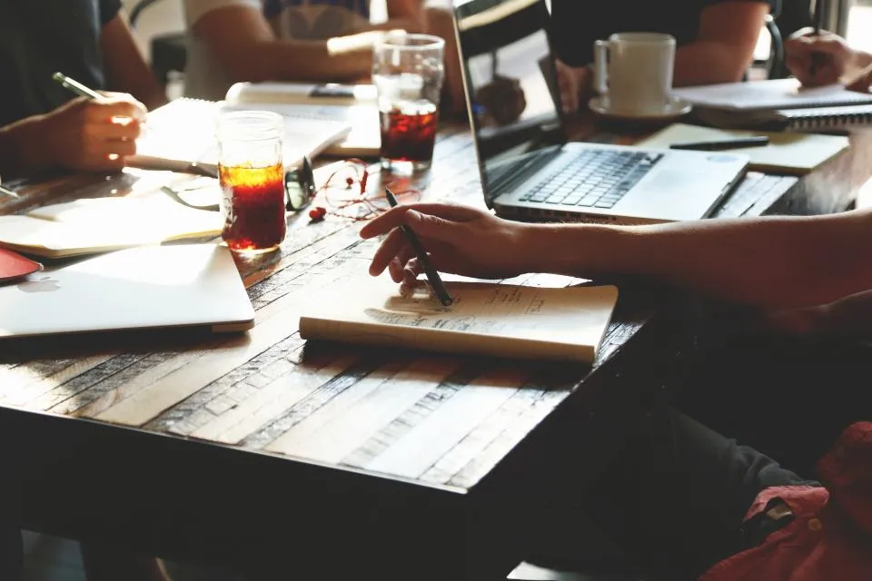 A team working around a wooden table with notebooks and laptops