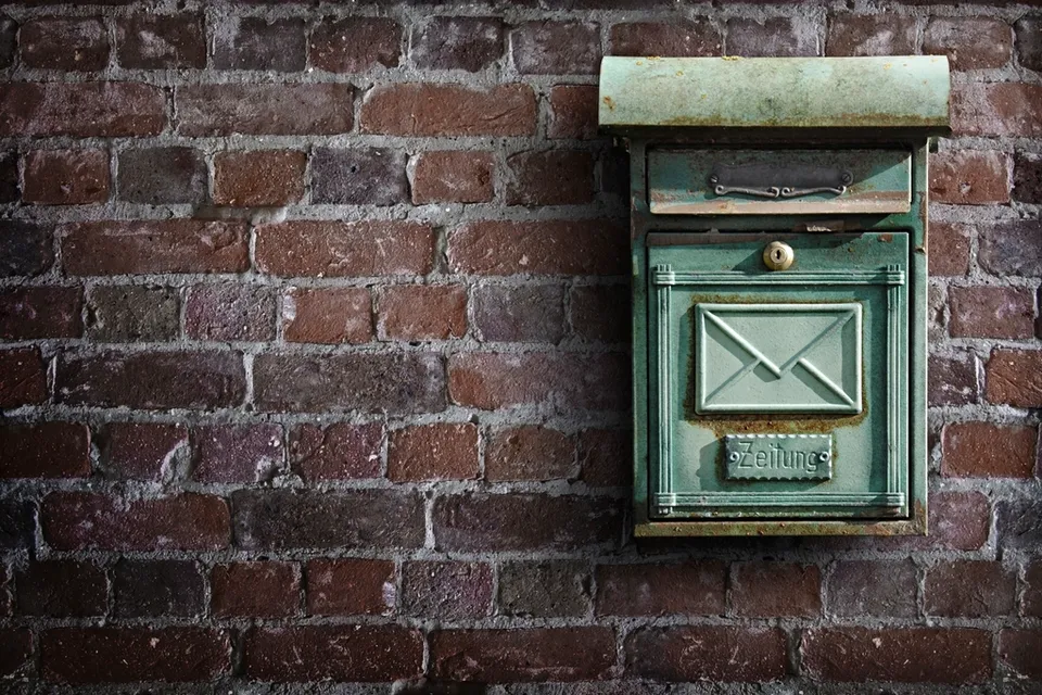 An old green letter box on a brick wall